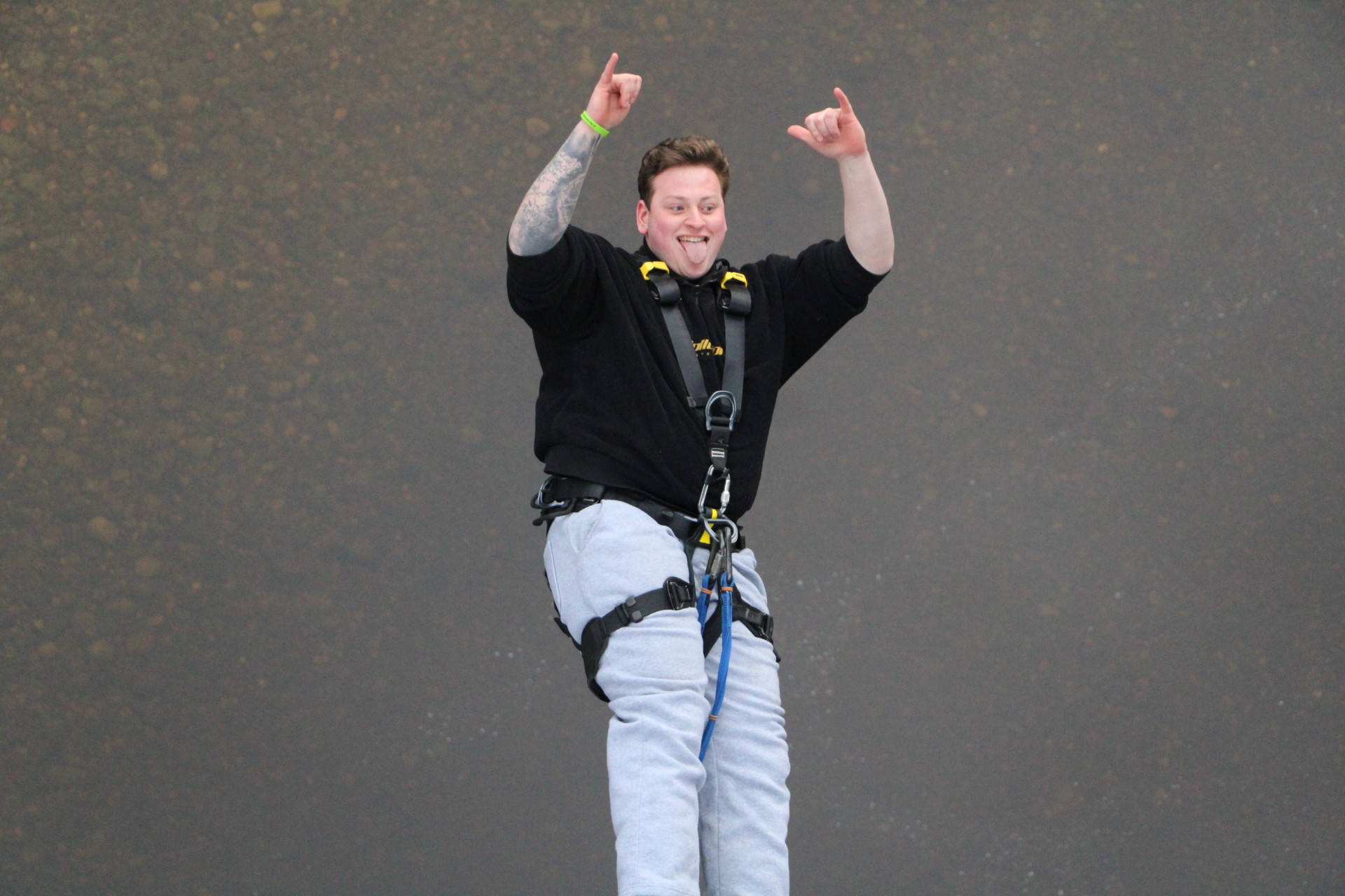 A picture of Adam during his bungee jump, smiling and arms in the air.